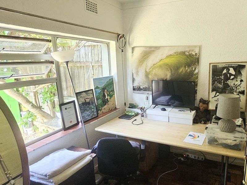 A functional home office space featuring parquet flooring and louvered windows overlooking the rear exterior area.