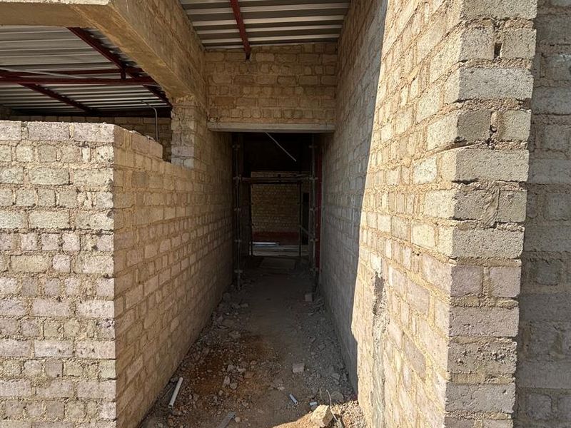 An unfinished hallway under construction featuring exposed brick walls and a steel roof structure, currently in a shell state.