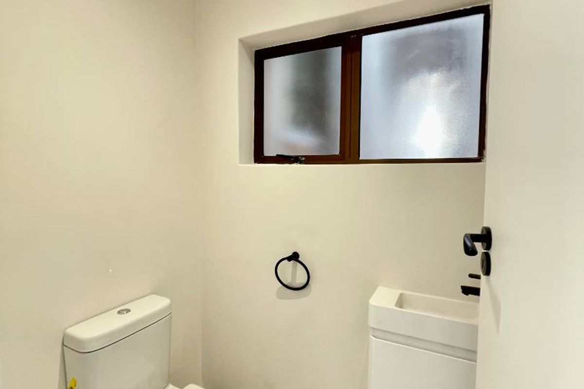 A compact guest bathroom featuring a modern toilet, a small wall-mounted vanity basin, and a frosted window for privacy.