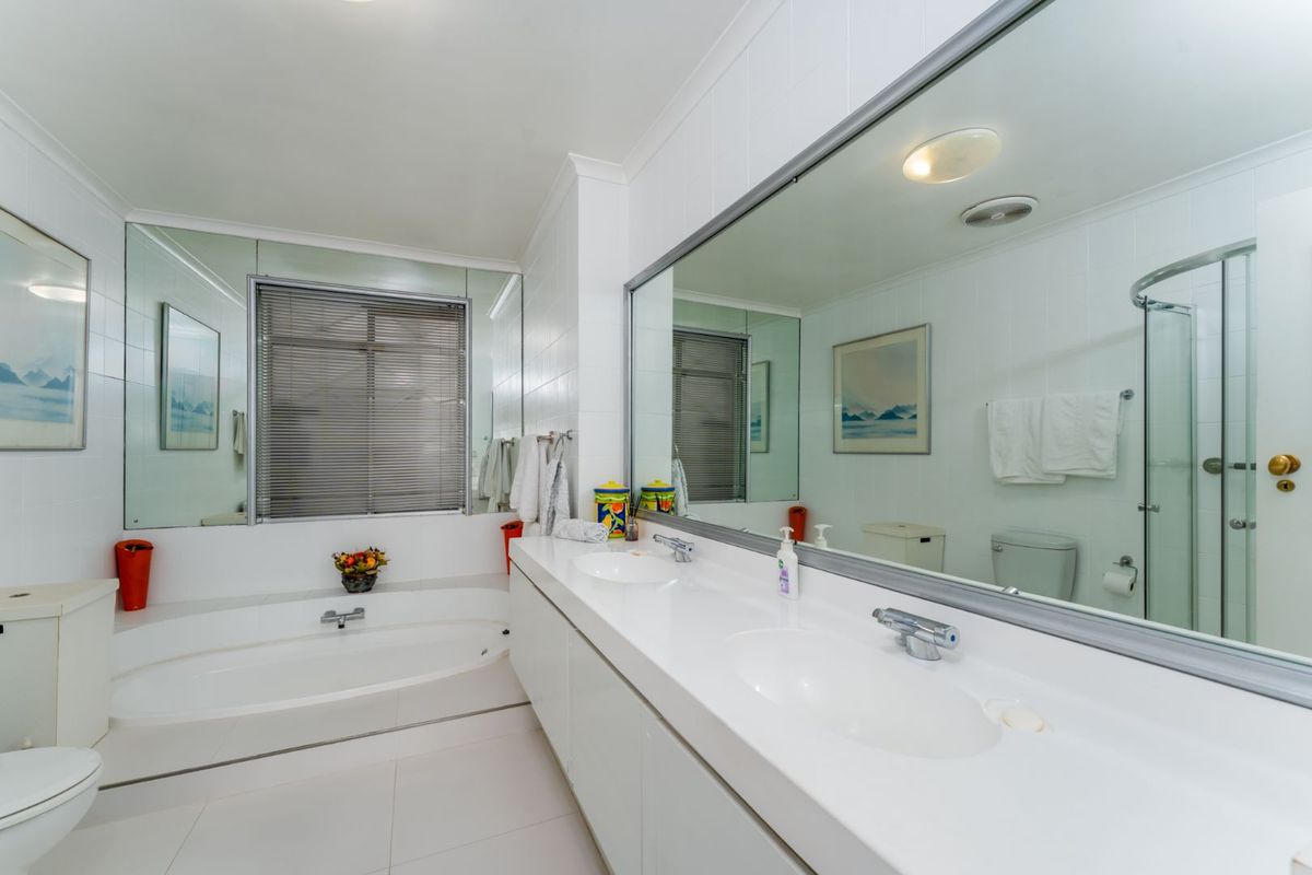 A functional bathroom featuring a dual-sink vanity, a built-in bathtub, and a separate shower enclosure with white tiled walls and large vanity mirrors.