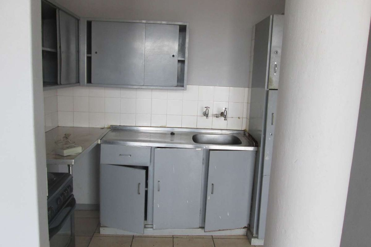 A dated kitchen area featuring original built-in cabinetry, a stainless steel sink, tiled backsplash, and tiled flooring, requiring modernization and repair.
