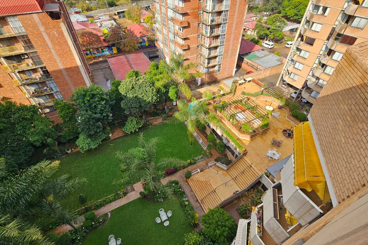 An elevated aerial view of the retirement village grounds, featuring landscaped gardens, paved walkways, and communal outdoor seating areas between residential apartment blocks.