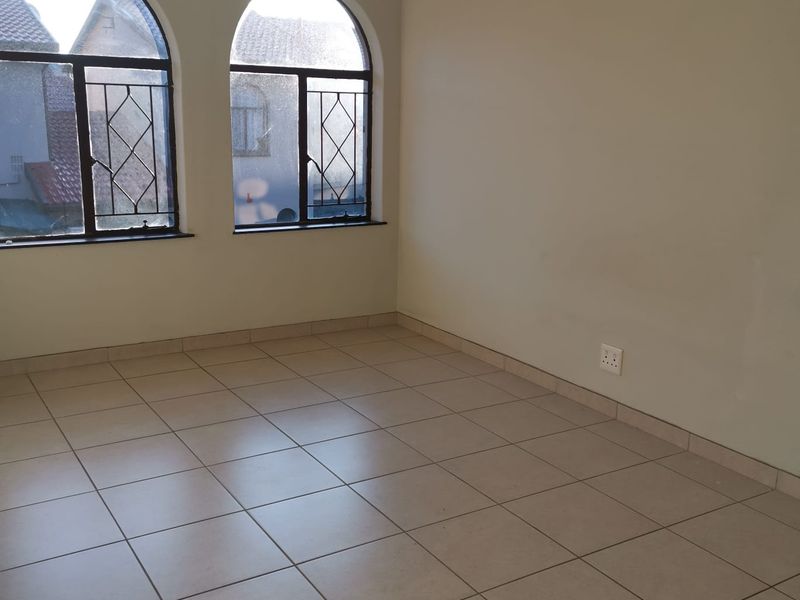 An empty living room featuring neutral tiled flooring and distinctive arched windows with security bars, offering a blank canvas for interior design.