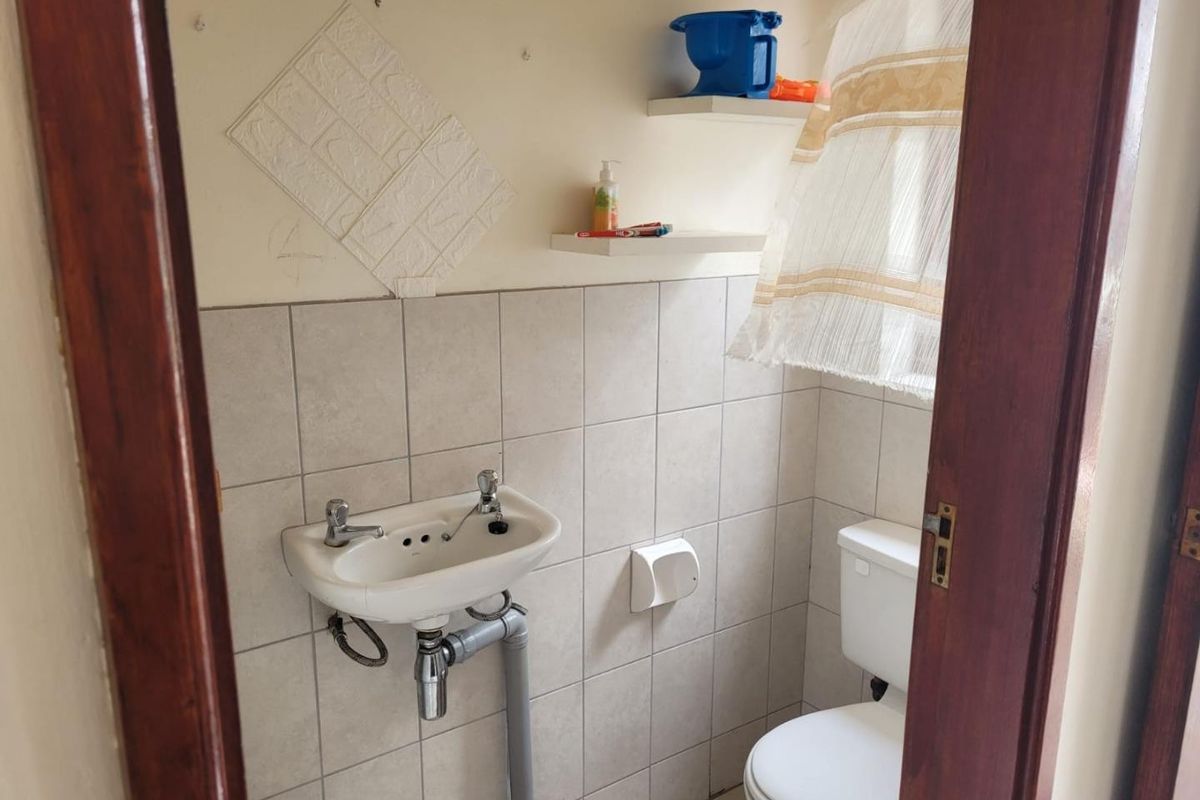 A compact guest bathroom featuring a wall-mounted basin, toilet, and tiled splashback, requiring cosmetic updates to improve the overall finish.