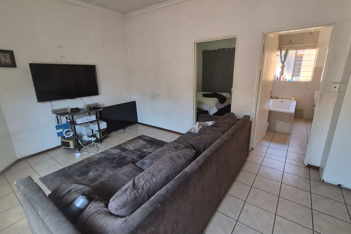 Living room area with tiled flooring, showing visible wear on wall surfaces, providing access to an adjacent bedroom and bathroom.