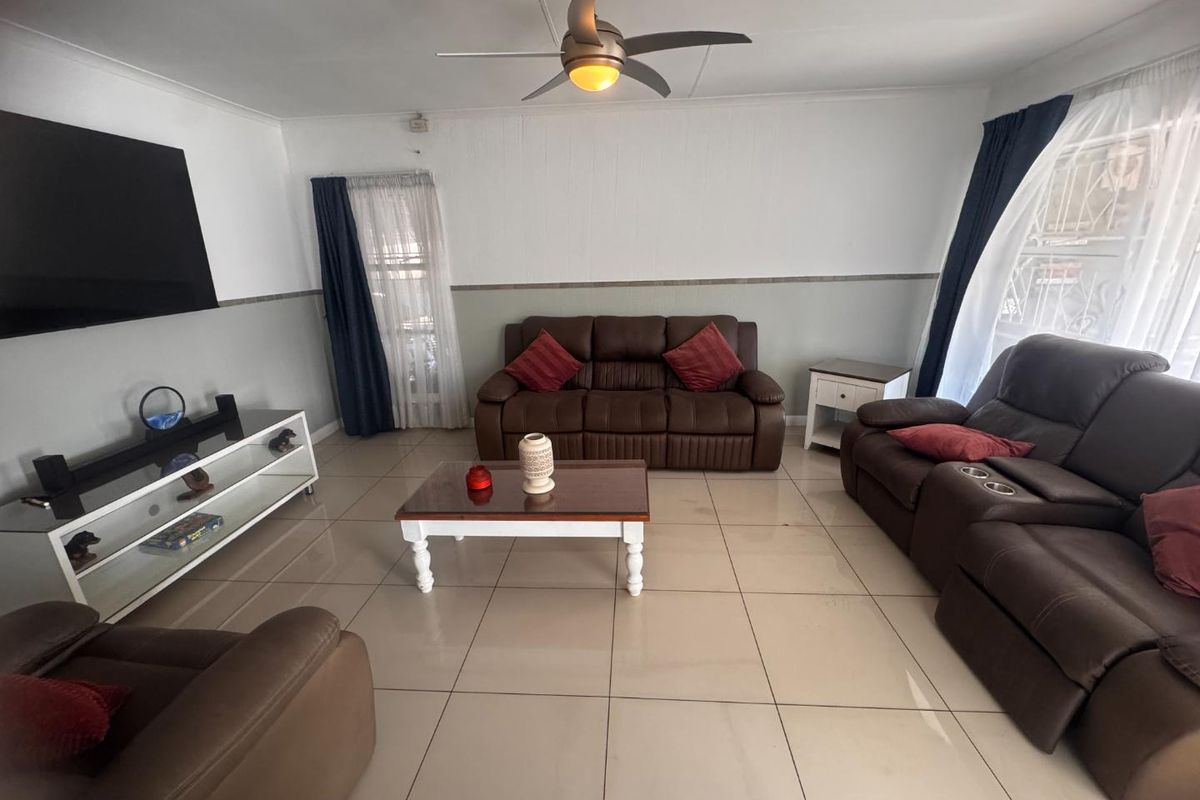 A spacious living room featuring neutral tiled flooring, a central ceiling fan, and a clean, well-maintained finish throughout the space.