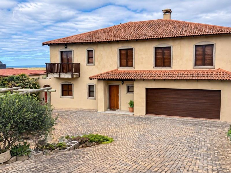 A well-maintained double-story house featuring a terracotta tiled roof, paved driveway, double garage, and a balcony with wooden shutters.