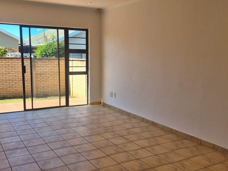 An empty, sunlit living room featuring neutral tiled flooring and a large sliding glass door providing direct access to the outdoor patio area.