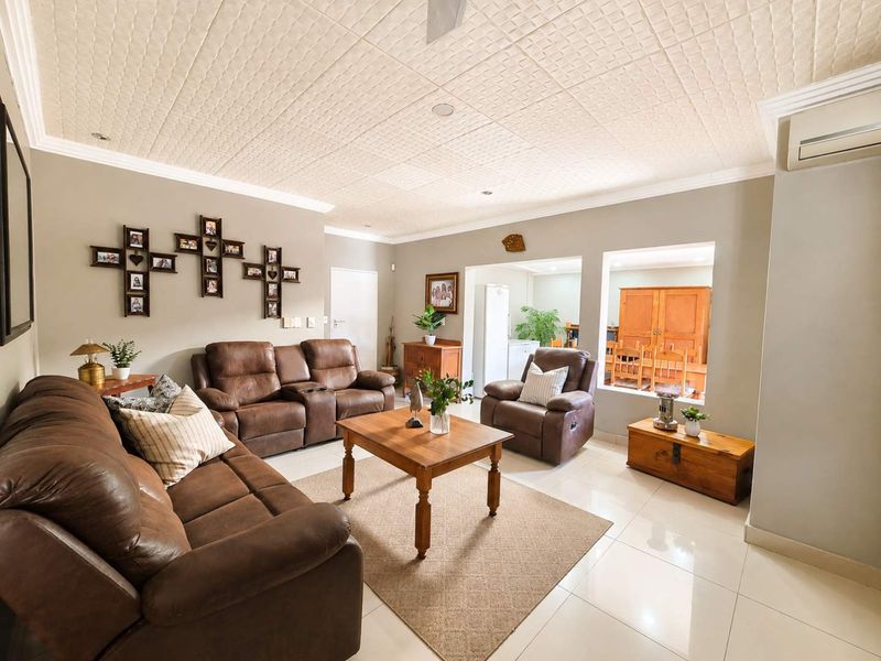 Spacious living room featuring tiled flooring, textured ceiling tiles, and a wall-mounted air conditioning unit, with an open flow to the adjacent dining area.
