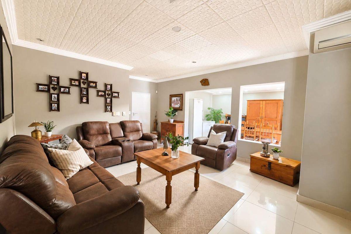 Spacious living room featuring tiled flooring, textured ceiling tiles, and a wall-mounted air conditioning unit, with an open flow to the adjacent dining area.