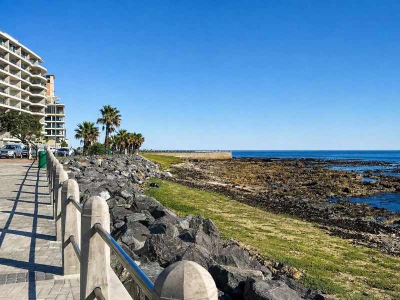 A scenic view of the coastal promenade and rocky shoreline adjacent to the apartment building, showcasing the prime seaside location.