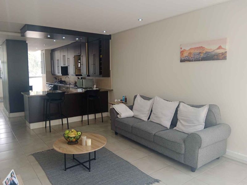 Open-plan living area featuring a modern kitchen with dark cabinetry, granite countertops, and tiled flooring throughout, creating a functional and cohesive space.