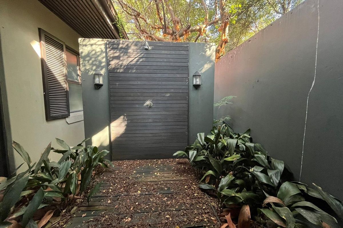Outdoor shower area featuring a timber-clad wall, wall-mounted lighting, and timber decking, enclosed by a private boundary wall.