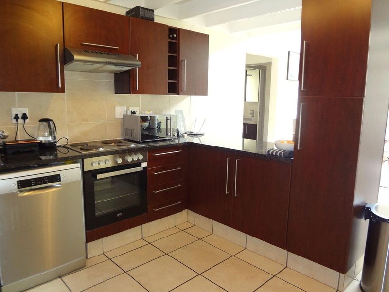A functional kitchen featuring dark wood cabinetry, granite countertops, a built-in oven, electric hob, and tiled flooring.