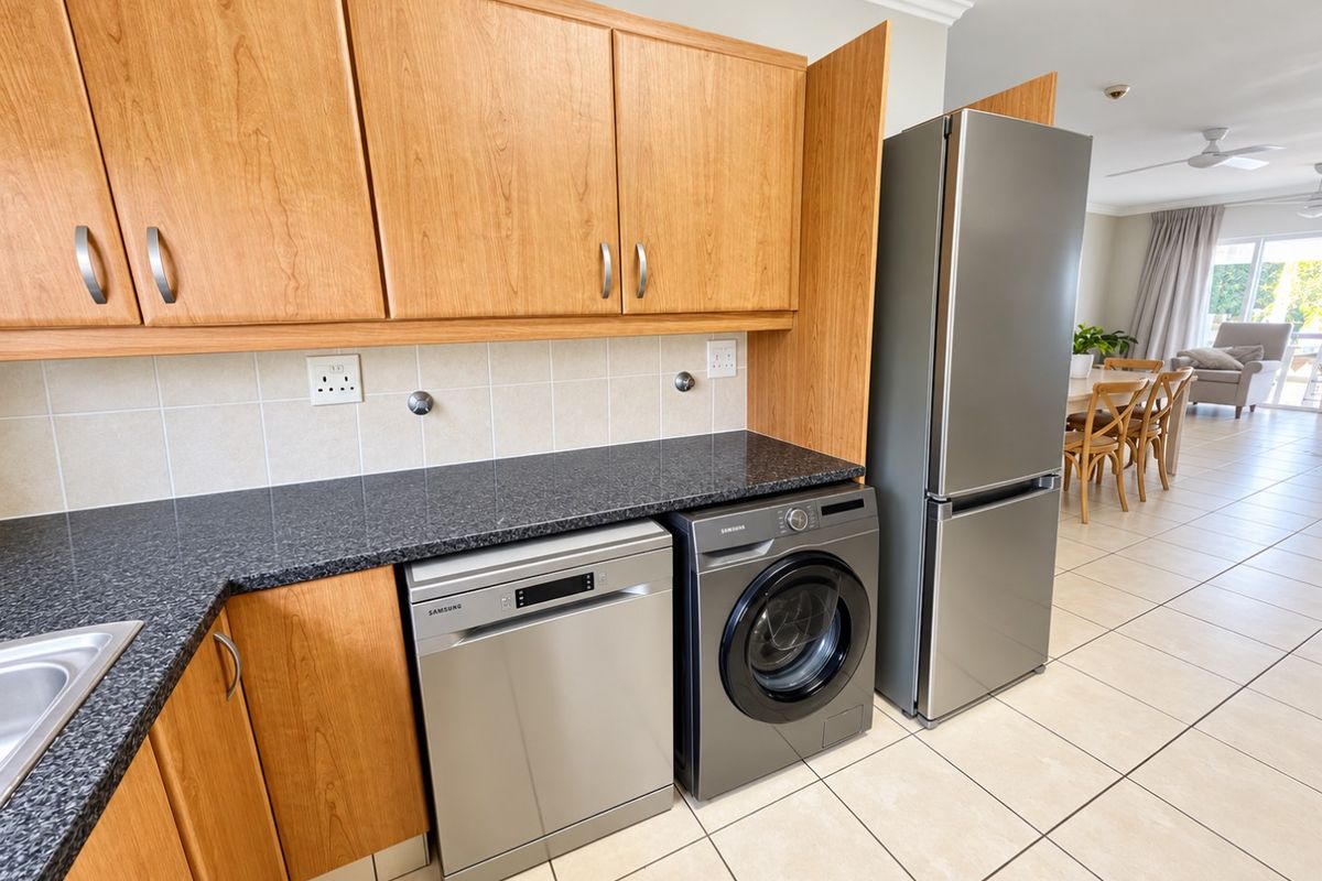 A functional kitchen featuring wood-look cabinetry, granite countertops, tiled backsplash, and tiled flooring, seamlessly flowing into the adjacent living and dining area.