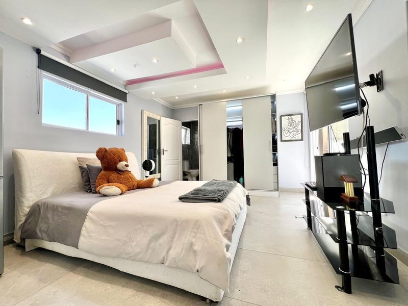 Modern bedroom featuring a recessed ceiling with ambient lighting, tiled flooring, and a built-in sliding door wardrobe with integrated en-suite access.