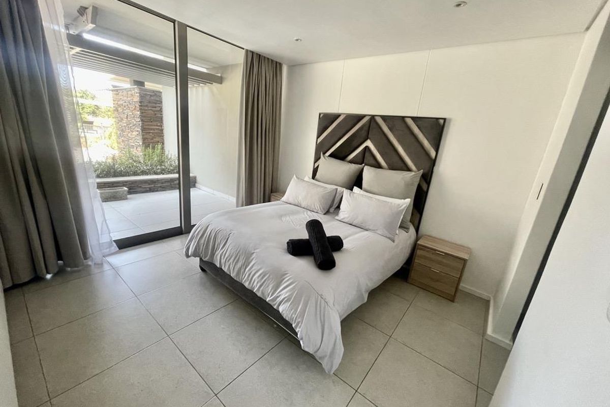Modern bedroom featuring large format floor tiles, recessed ceiling lighting, and floor-to-ceiling sliding glass doors providing direct access to a private patio.