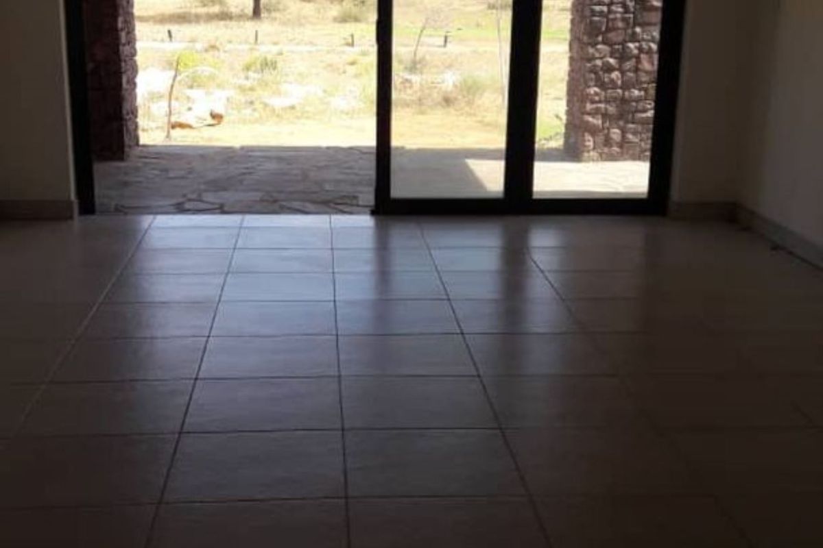 An empty living area featuring large sliding glass doors that open onto a stone-paved patio with views of the surrounding landscape.