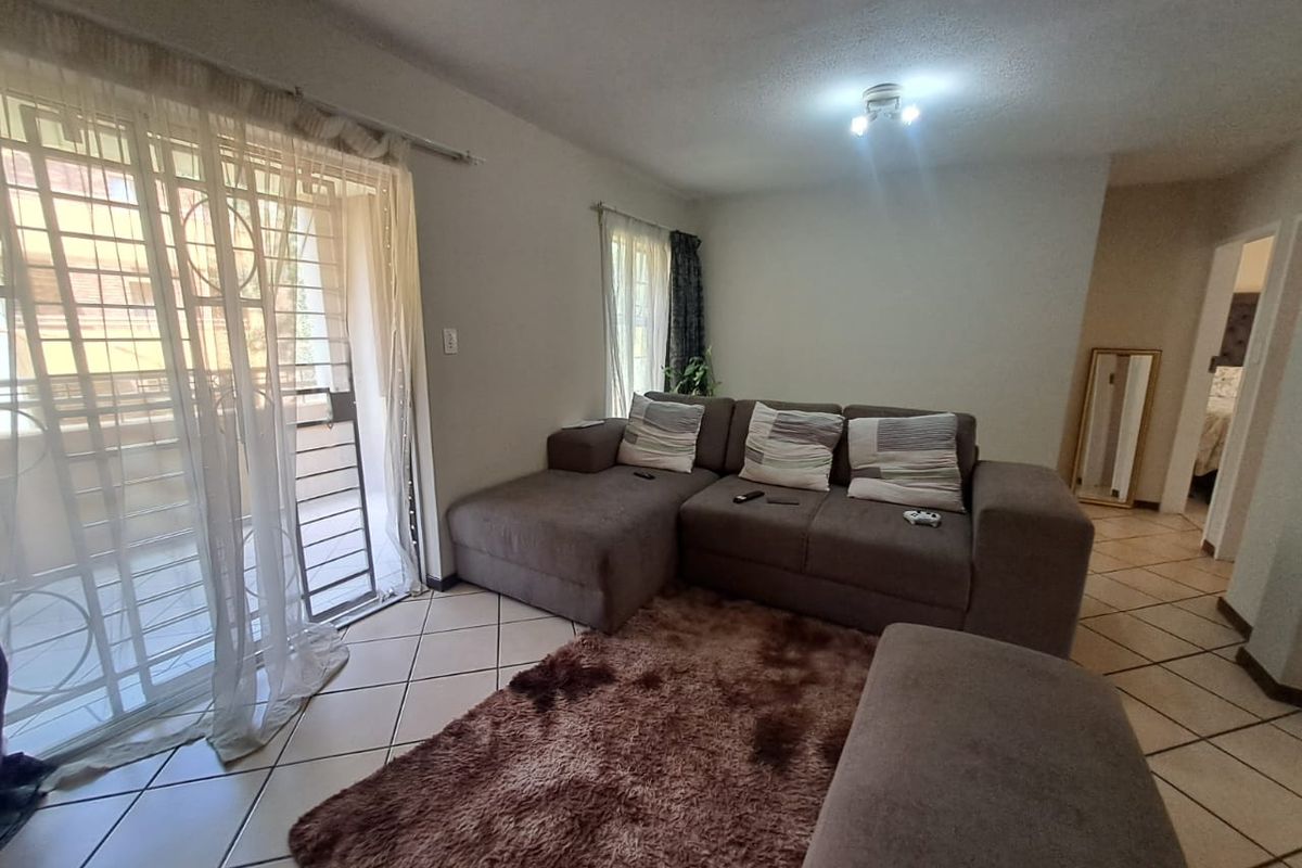 A living room featuring tiled flooring and a sliding glass door with security gate, providing access to an outdoor balcony area.