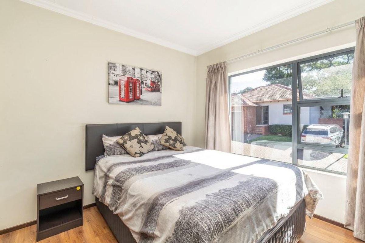 A bright bedroom featuring laminate flooring, coving, and a large window providing natural light and a view of the exterior.