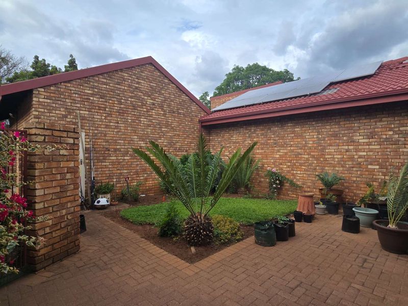 A private rear courtyard featuring face brick walls, a paved patio area, a small lawn, and roof-mounted solar panels.
