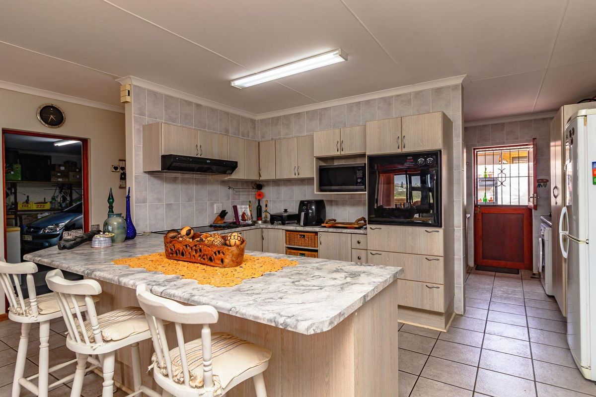 A functional kitchen featuring light wood-tone cabinetry, a marble-effect breakfast bar, built-in oven, extractor fan, and tiled flooring with direct access to the rear.
