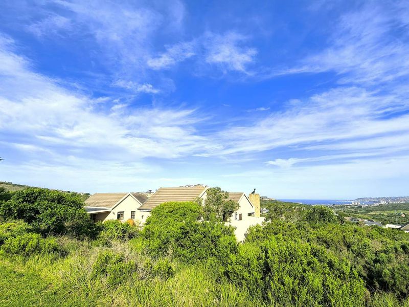 A scenic elevated view of the property exterior, showcasing the surrounding landscape, natural vegetation, and distant coastal horizon under a clear blue sky.