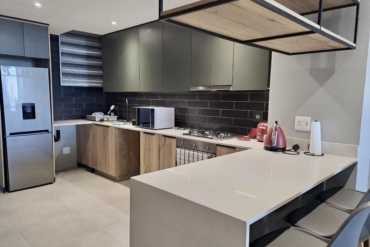 Modern kitchen featuring sleek dark cabinetry, stone countertops, a breakfast bar, gas hob, and integrated appliances with a contemporary subway tile backsplash.