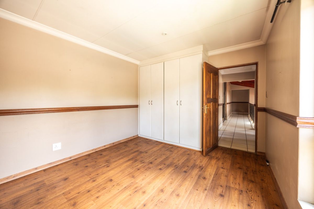 An empty bedroom featuring laminate flooring, built-in cupboards, and a wooden dado rail, offering a neutral canvas for personalization.
