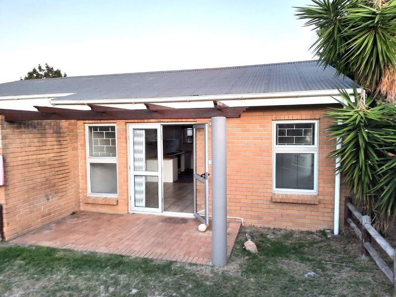 Rear exterior view of the house featuring a brick facade, corrugated metal roof, timber pergola, and a paved patio area with access to the interior.