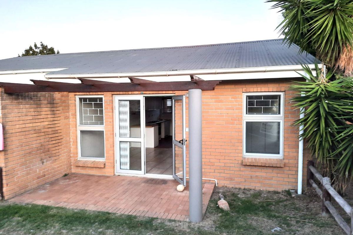 Rear exterior view of the house featuring a brick facade, corrugated metal roof, timber pergola, and a paved patio area with access to the interior.