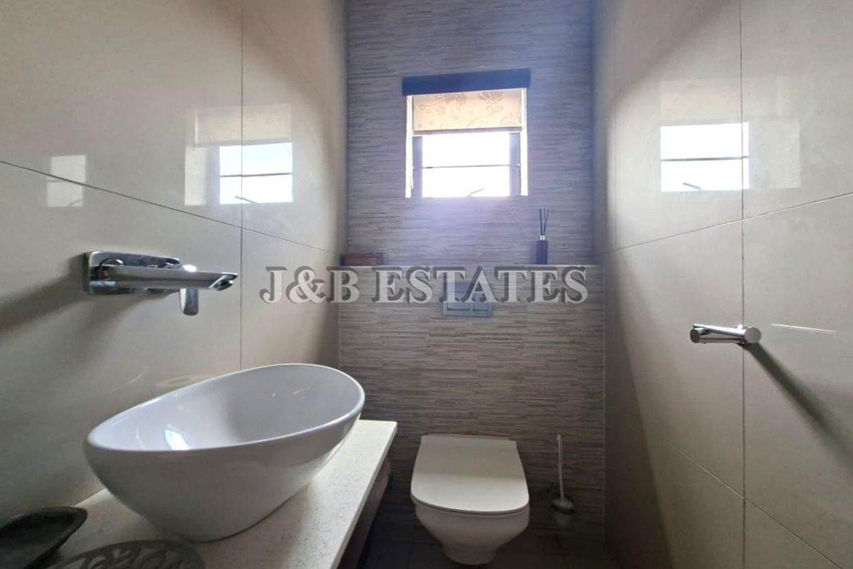 A modern guest bathroom featuring a wall-mounted toilet, a vessel sink on a stone vanity, and contemporary tiled walls.