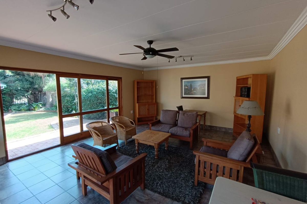 Spacious living room featuring large sliding glass doors that open to the garden, tiled flooring, and a ceiling fan.