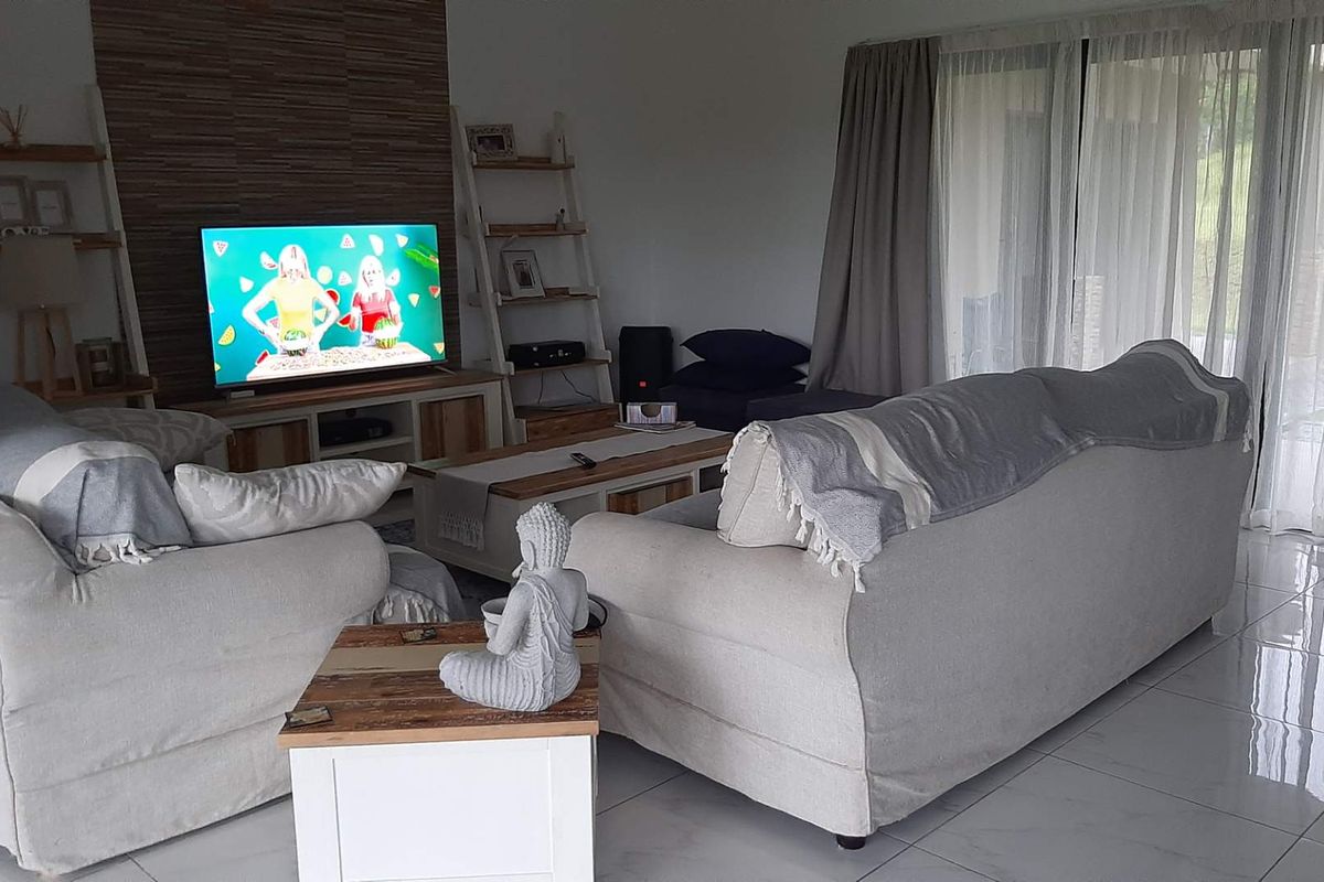 A comfortable living room featuring tiled flooring, a textured feature wall, and large sliding glass doors providing natural light and garden access.
