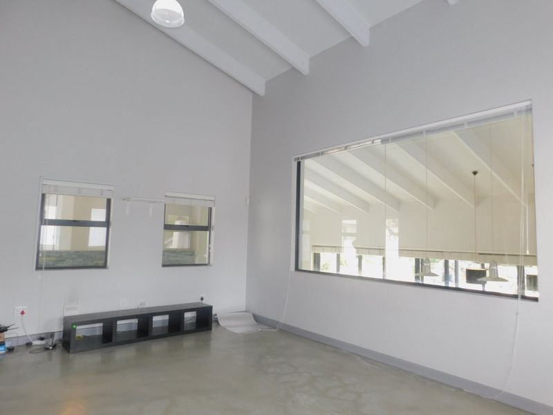 Spacious living area featuring high vaulted ceilings with exposed rafters, polished concrete floors, and large windows providing ample natural light.