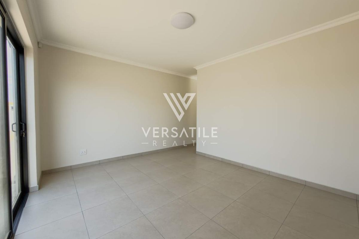 A bright, empty living area featuring neutral tiled flooring, clean walls, and a sliding glass door providing access to the exterior.