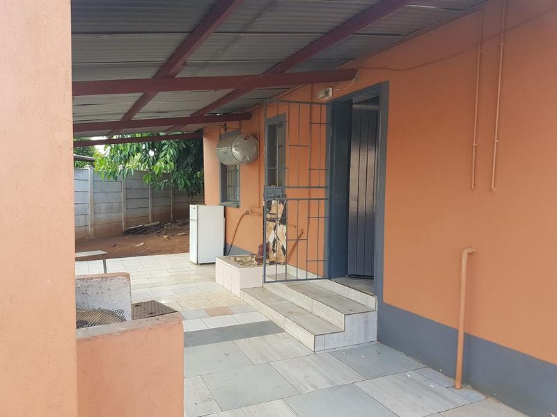 Covered outdoor patio area featuring tiled flooring, a built-in braai, and direct access to the home via a security gate.