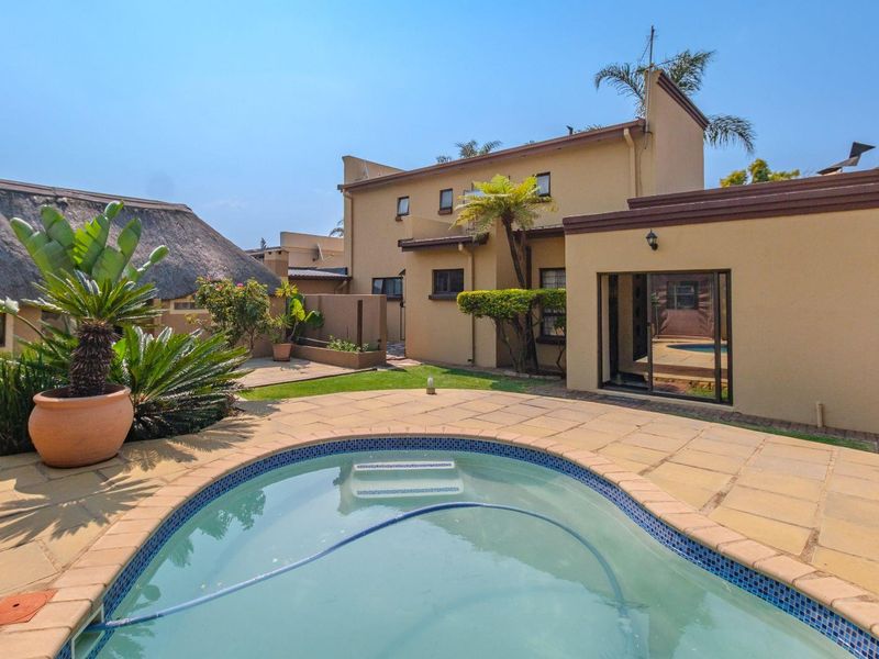 Rear exterior view featuring a swimming pool with sandstone coping, paved patio area, and access to the main dwelling via sliding glass doors.