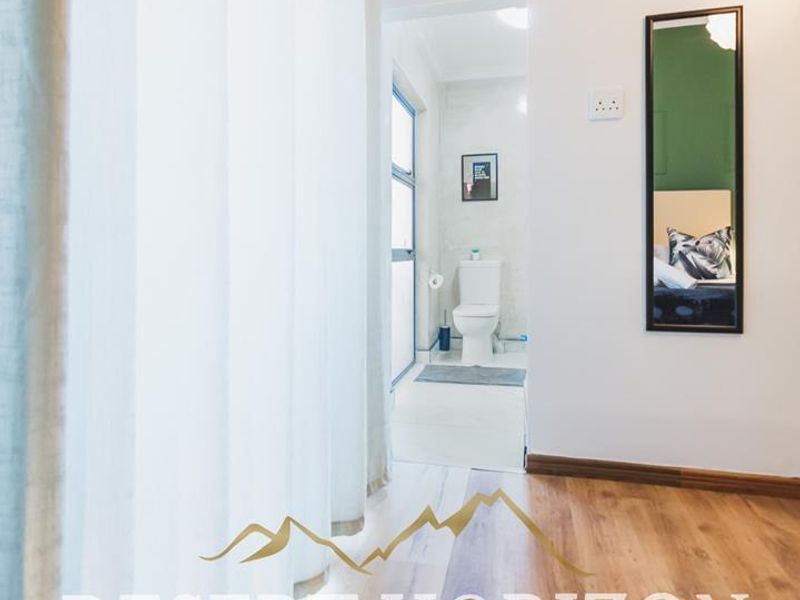 A bedroom featuring laminate flooring and coving, with a direct view into an en-suite bathroom.