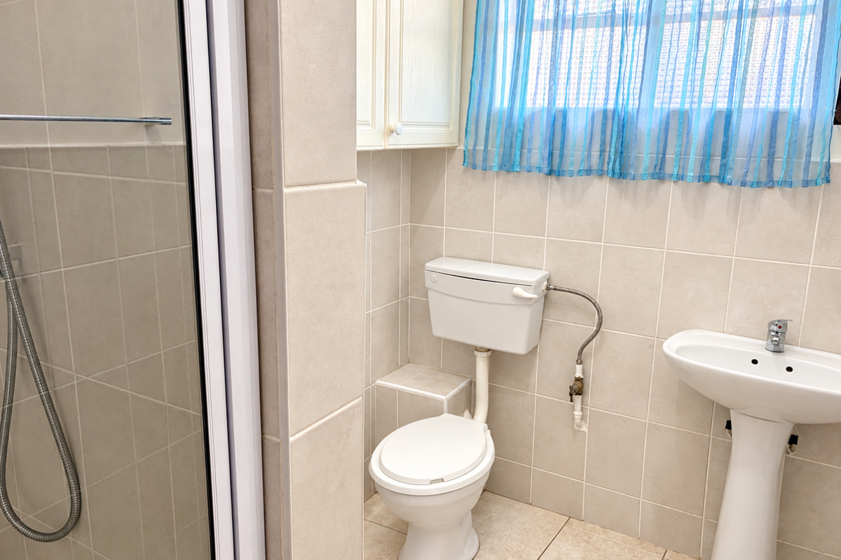 A functional bathroom featuring a shower enclosure, pedestal basin, and toilet with neutral wall and floor tiling.