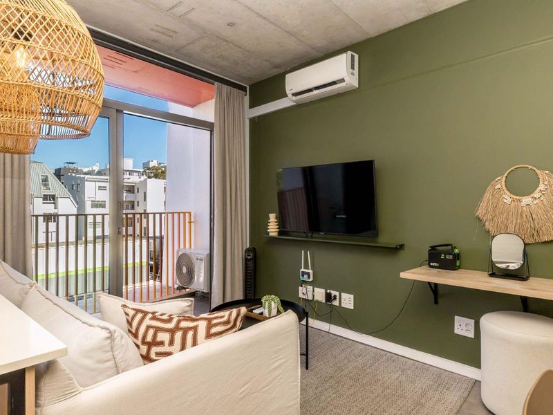Modern living area featuring an exposed concrete ceiling, olive green accent wall, split-system air conditioning, and direct access to a private balcony.