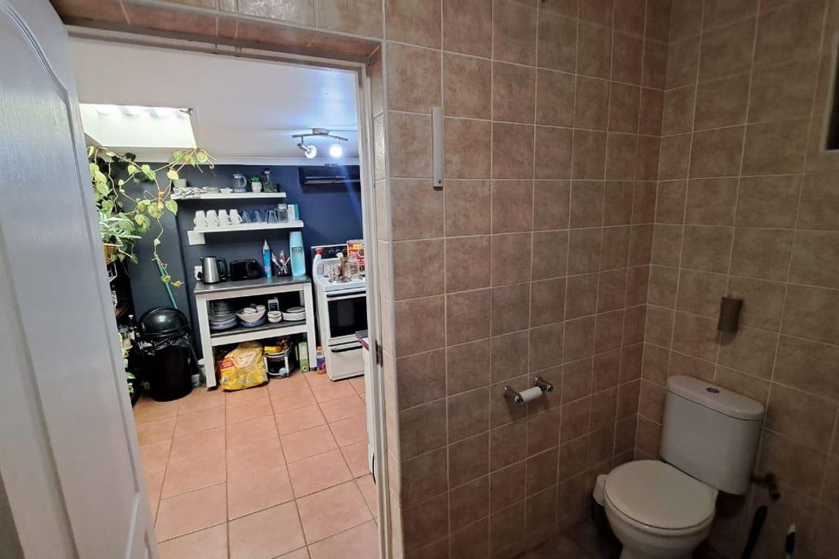 A functional bathroom featuring full-height wall tiling and a standard toilet, with a direct view into the adjacent kitchen area.