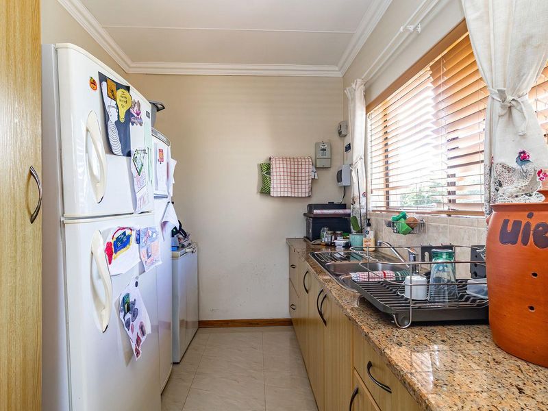 A functional kitchen featuring granite countertops, stainless steel sink, and ample built-in cabinetry with tiled flooring and natural light from the window.