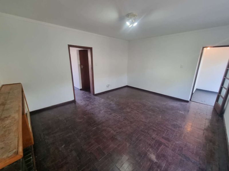 An empty living room featuring original parquet flooring and neutral walls, offering a blank canvas for renovation or interior design updates.