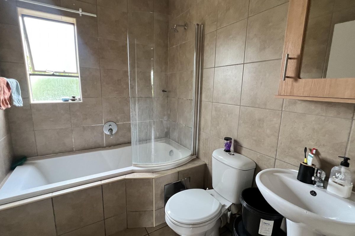 A functional bathroom featuring tiled walls and flooring, a built-in bathtub with a glass shower screen, a pedestal sink, and a wall-mounted medicine cabinet.