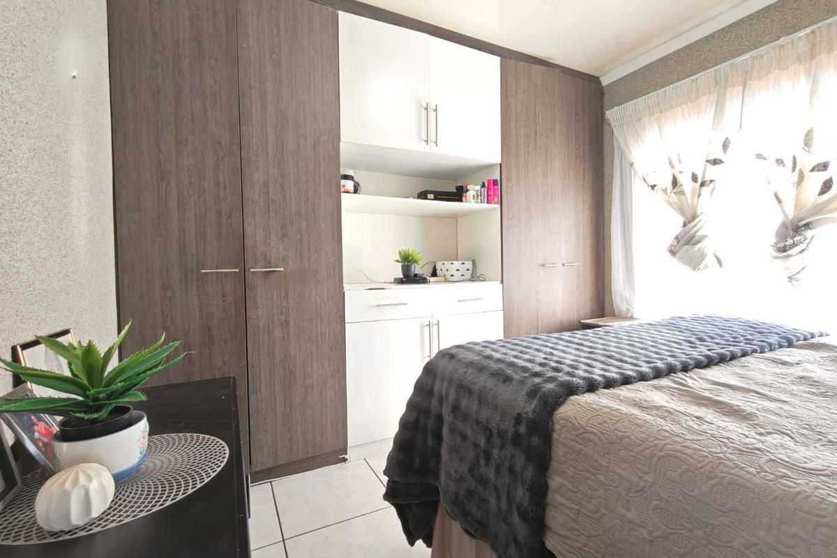 A bedroom featuring modern built-in cupboards with a mix of wood-grain and white finishes, complemented by neutral tiled flooring.