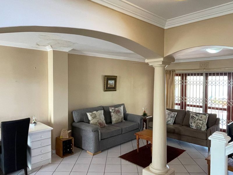 Spacious living area featuring an arched entryway, decorative column, tiled flooring, and sliding glass doors with security gates leading to the exterior.