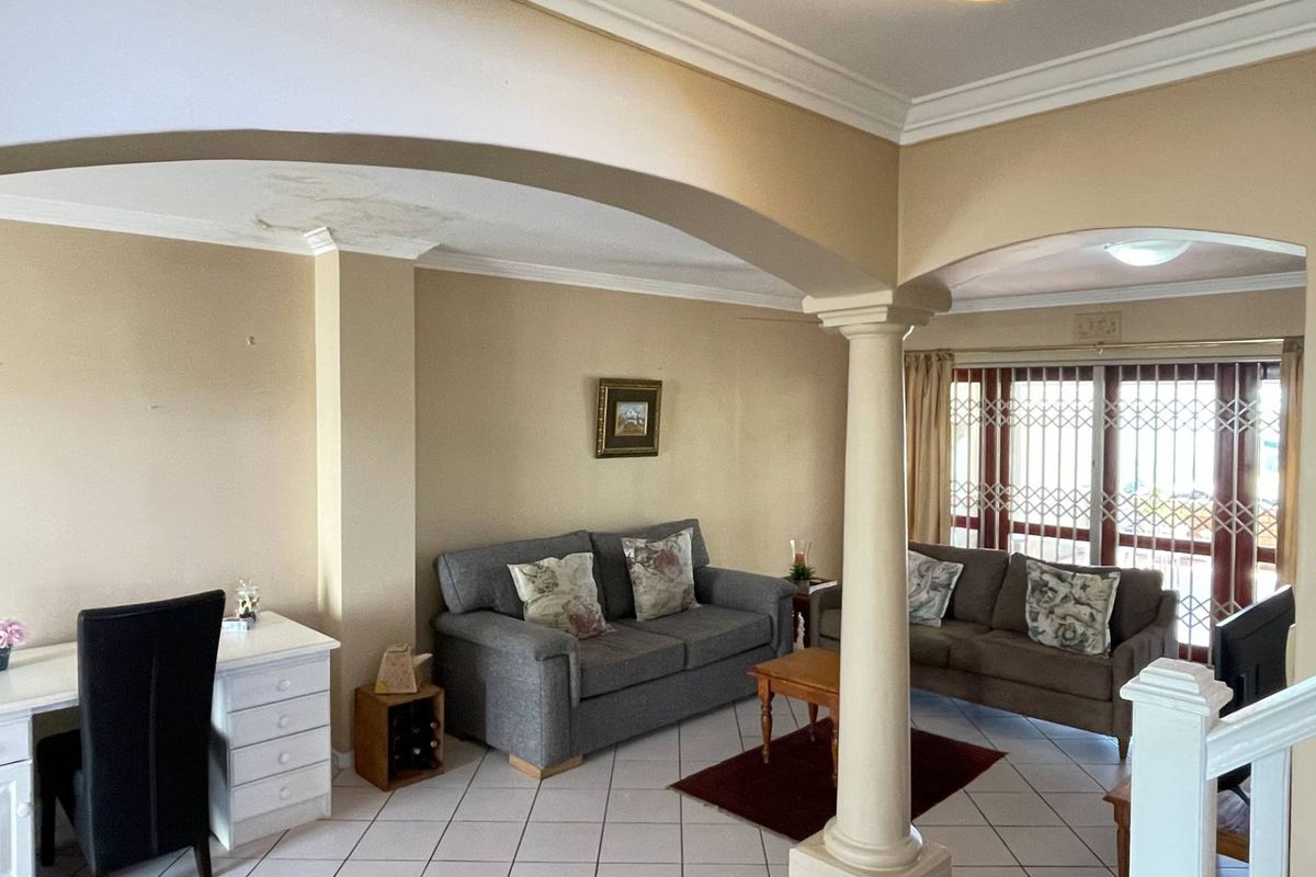 Spacious living area featuring an arched entryway, decorative column, tiled flooring, and sliding glass doors with security gates leading to the exterior.