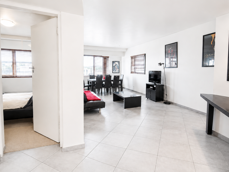 Spacious open-plan living and dining area featuring neutral tiled flooring, recessed lighting, and direct access to an adjacent bedroom.