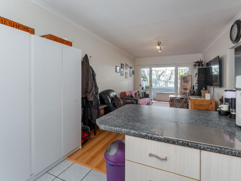 Open-plan living area featuring a kitchen island with stone-look countertop, transitioning from tiled kitchen flooring to laminate living area flooring with access to a balcony.
